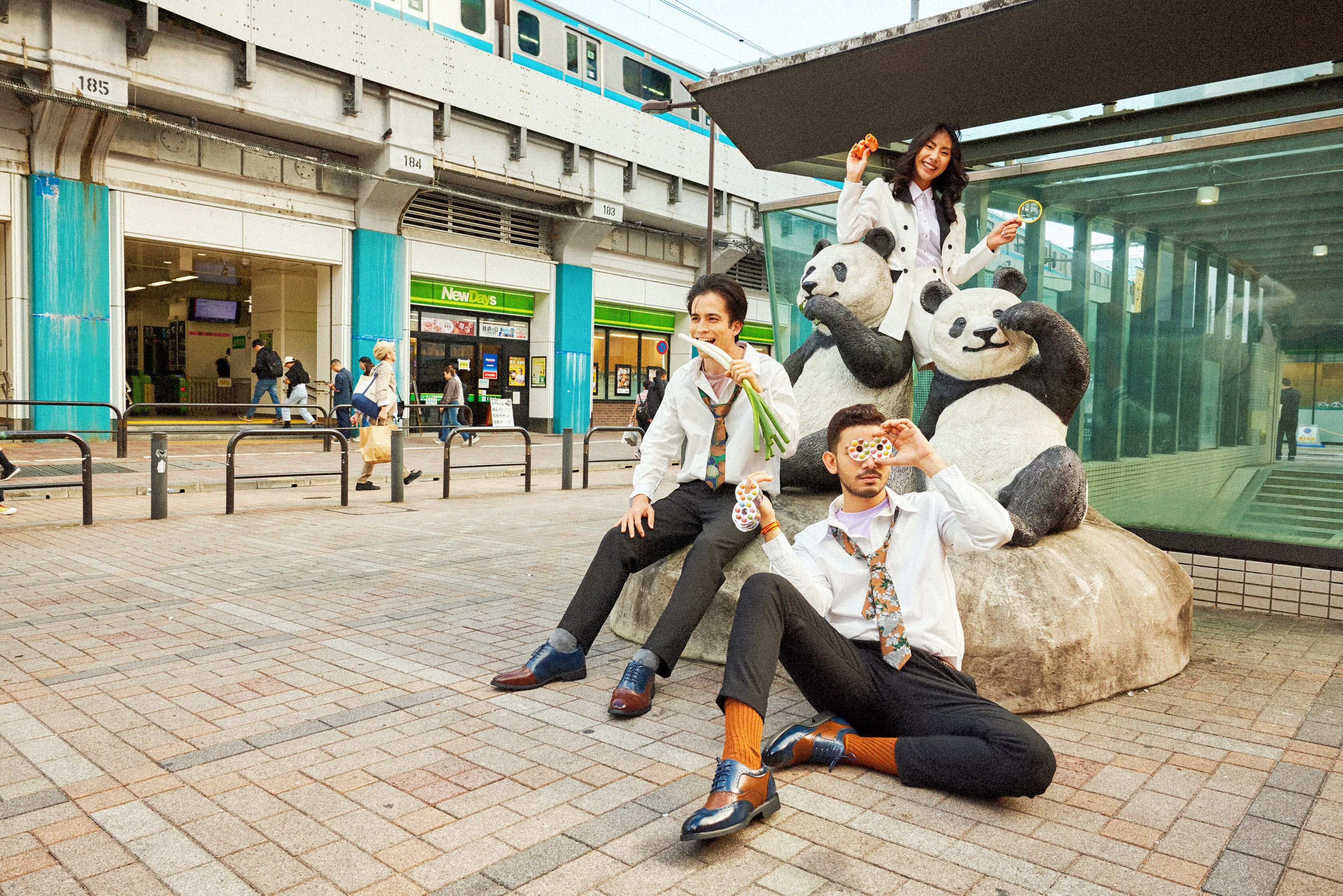 A public square with a large panda statue, people sitting and standing, and a building with signage in the background.