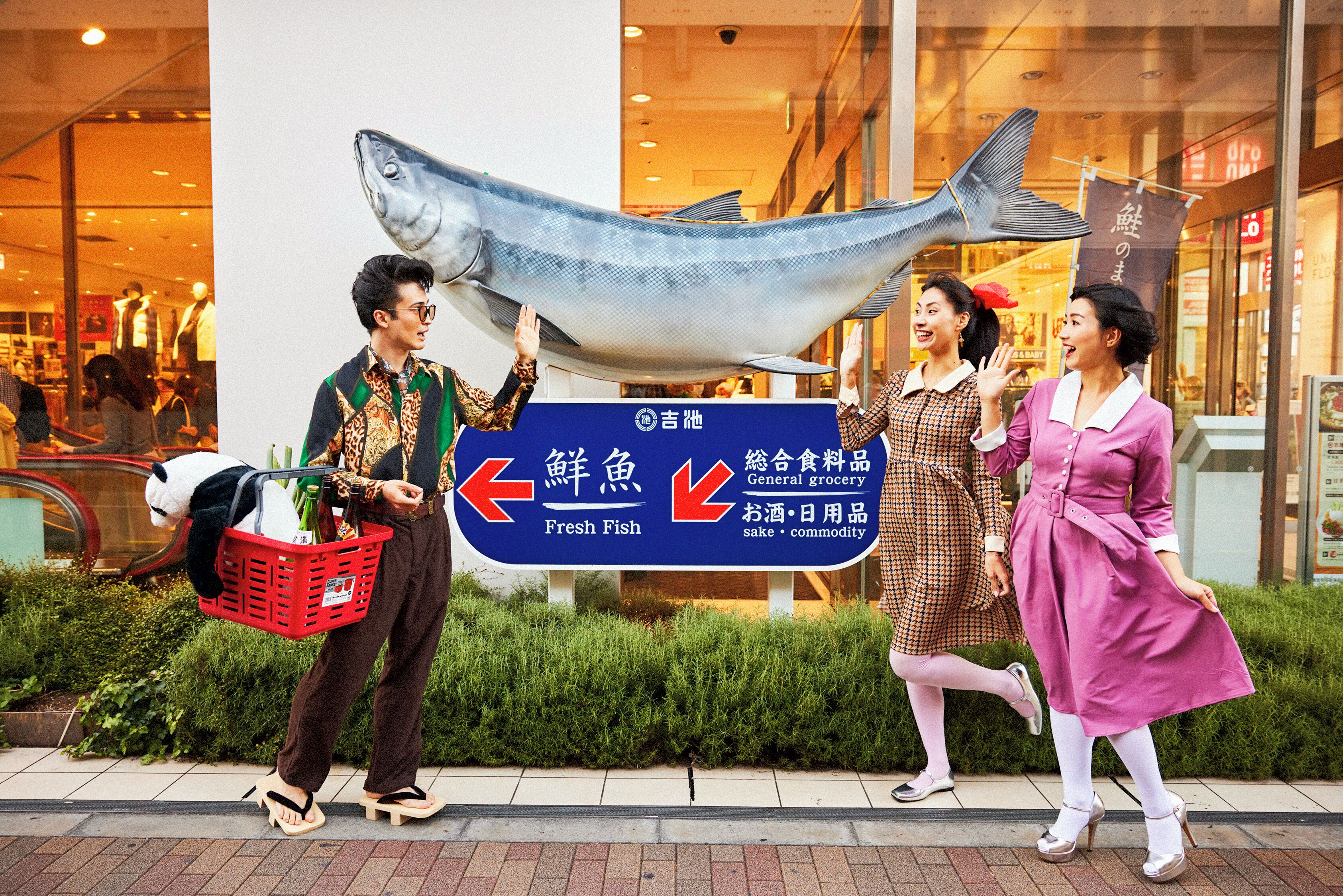 A street scene with a large fish sculpture, a sign pointing to Fresh Fish, and a general grocery store.