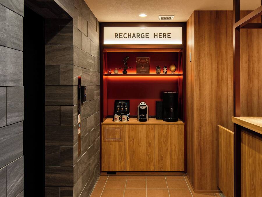A hotel room with a wooden cabinet, a sign that reads 'RECHARGE HERE', and a coffee machine.