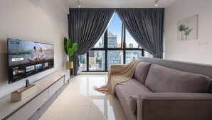 A modern living room with a large flat-screen TV, a sofa, a plant, and a city view through large windows. - Majestic by Avery &10 mins to Twin Tower (Kuala Lumpur)