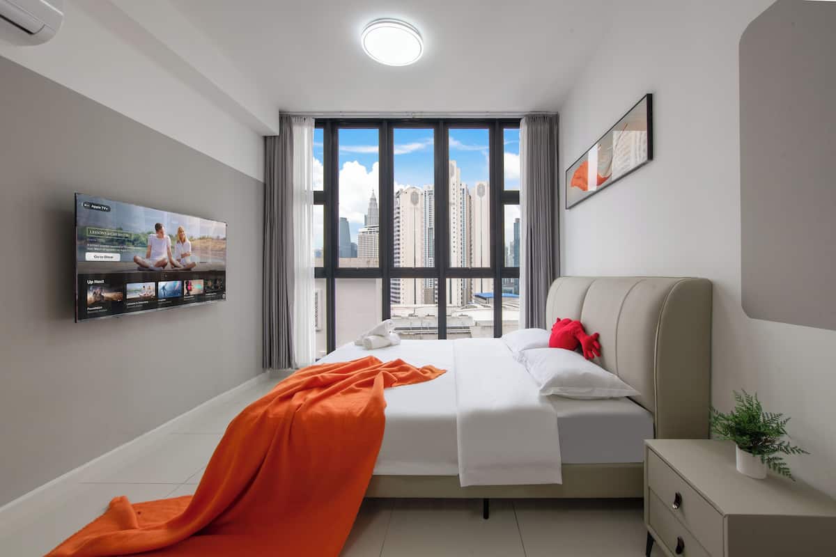A modern hotel room with a large window, a bed, a bedside table, a TV, and a potted plant.