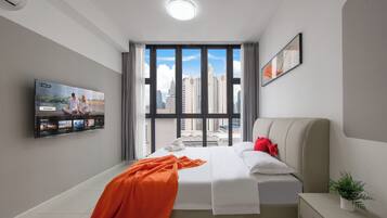 A modern hotel room with a large window, a bed, a bedside table, a TV, and a potted plant.