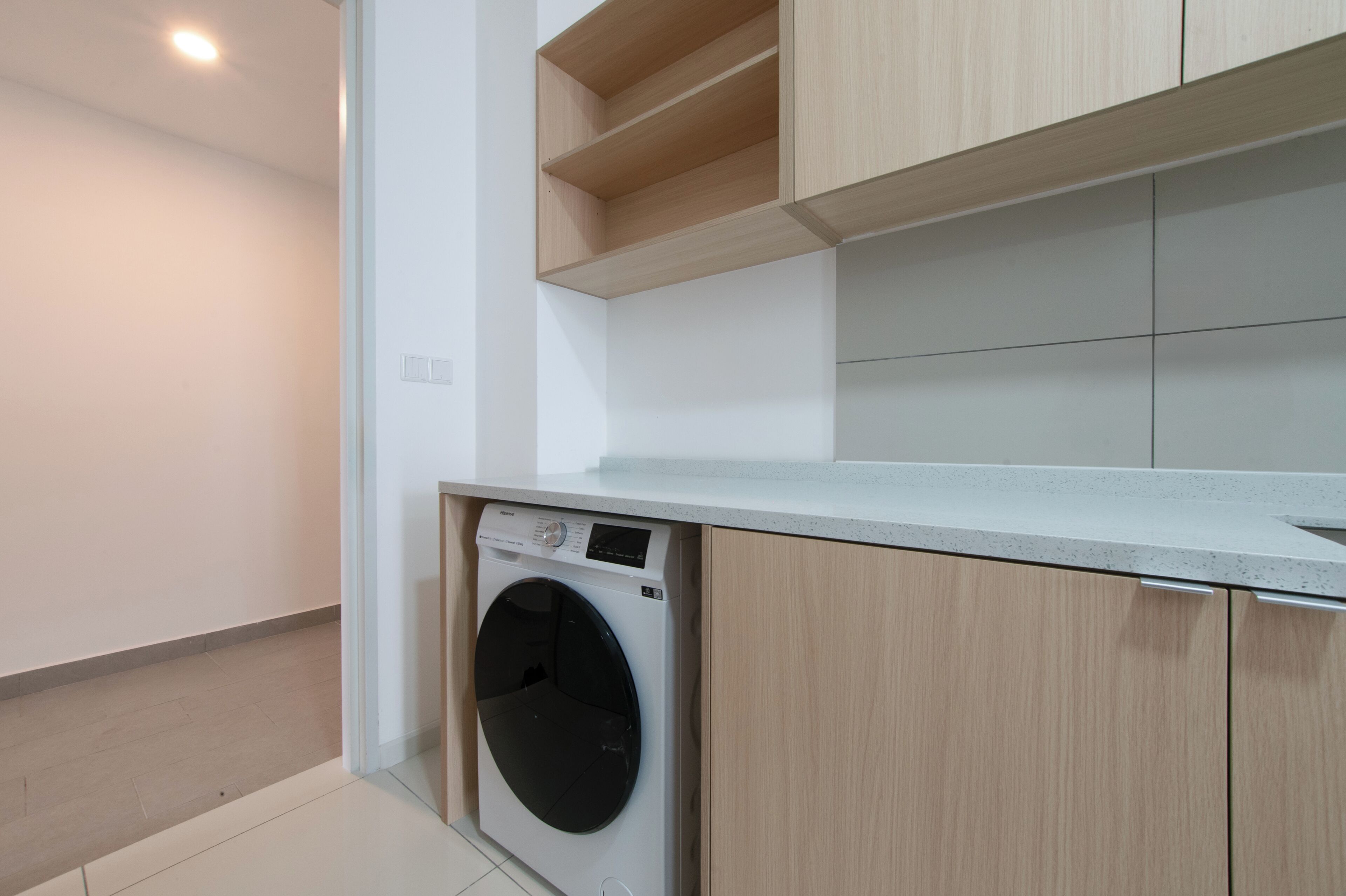 Een compacte keuken met een ingebouwde wasmachine, houten kastjes en een betegelde spatwand.