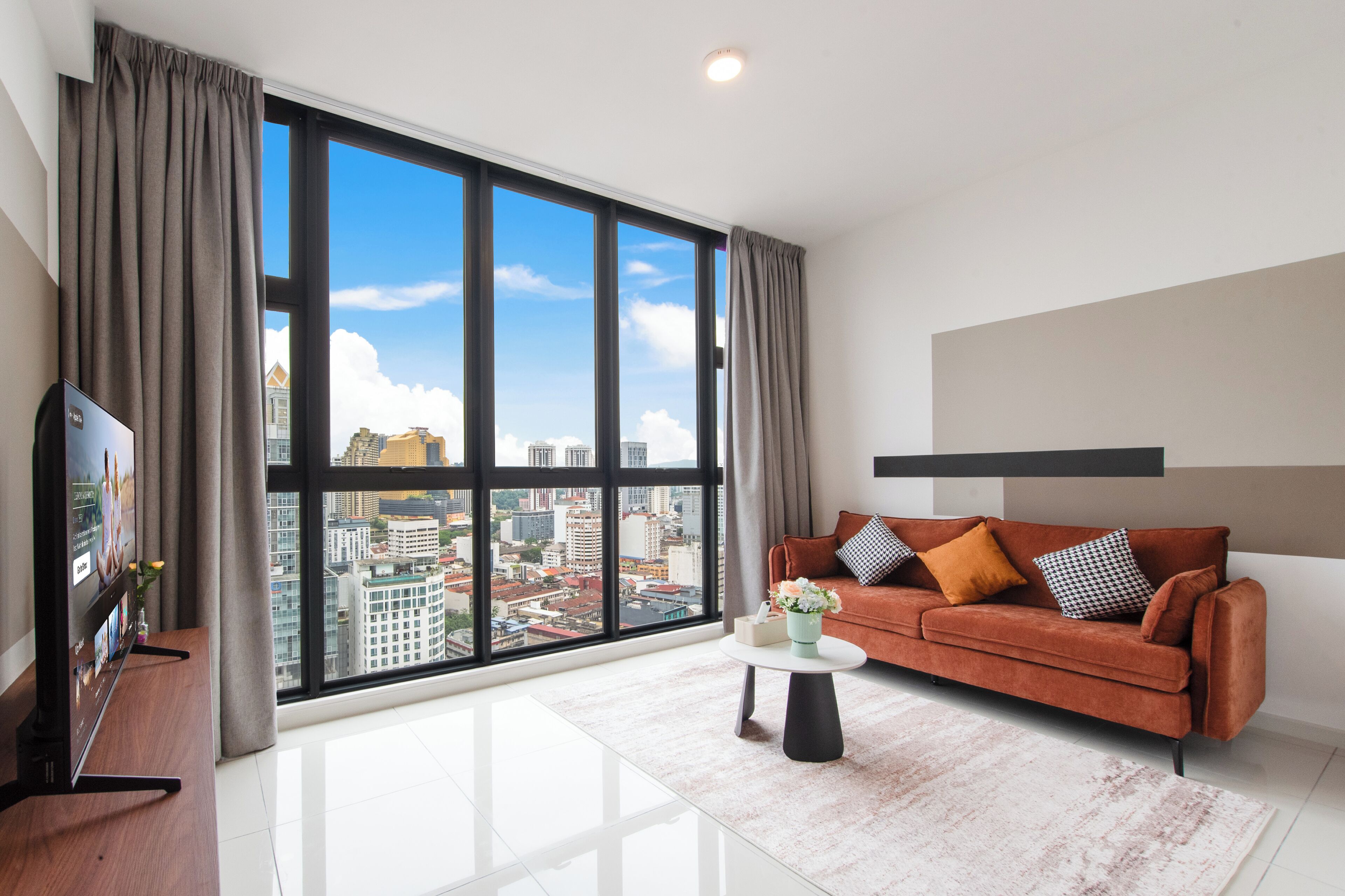 A modern living room with a large window, a sofa, a coffee table, and a flat-screen TV.