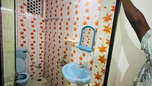 A small bathroom with a toilet, sink, and mirror. The walls are decorated with a floral pattern. - Hotel Sai Deep Place (Baga)