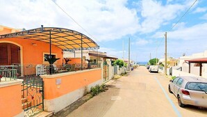 A street with houses, a covered outdoor area, and parked cars.