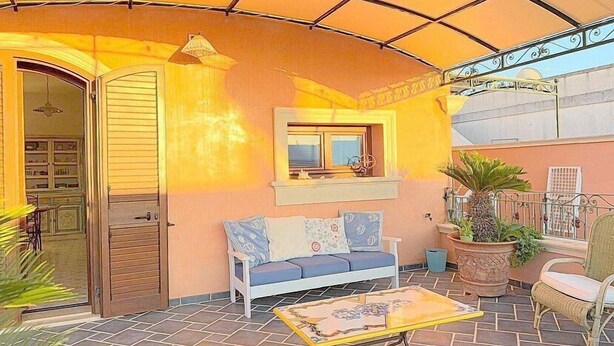 A covered patio area with a sofa, a small table, and potted plants.