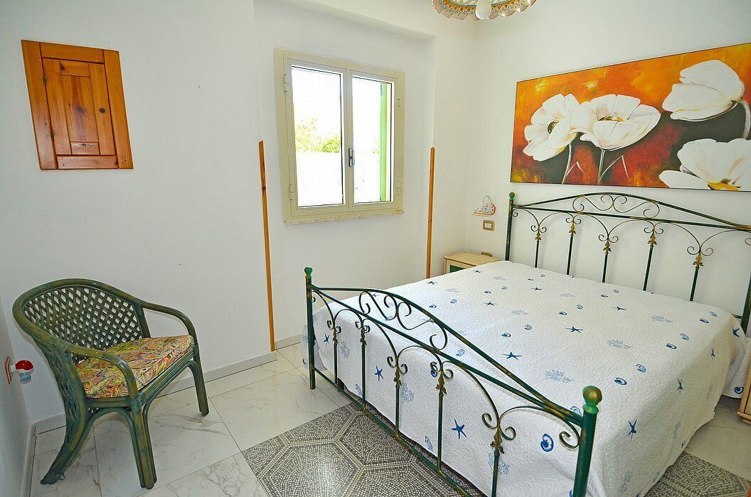 Quarto com cama, cadeira, janela e um quadro na parede.