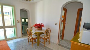 A dining area with a table and chairs, a vase of red flowers, and a kitchen visible through an open door. - Casa Nima: A welcoming independent house situated at a short distance from the beach, with Free WI-FI. (Patù)