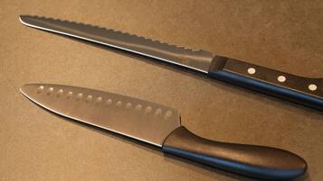 Two kitchen knives with blue handles on a brown countertop.
