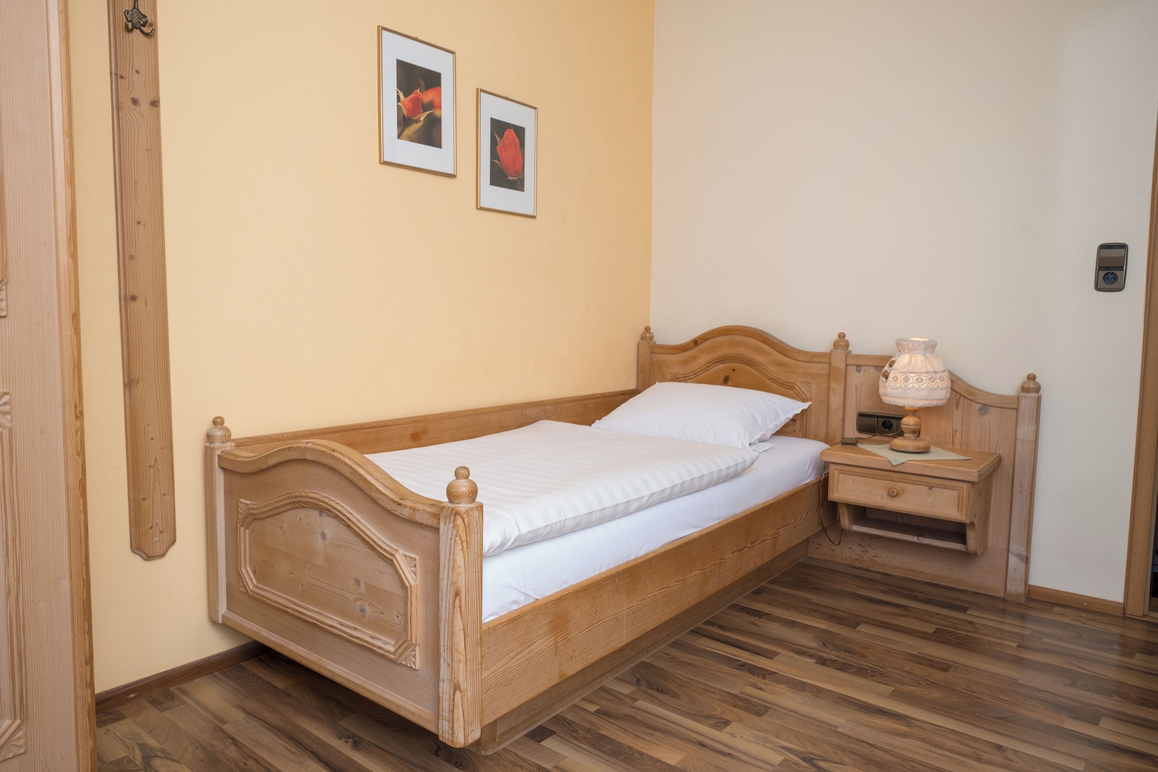 A wooden bed with a headboard, a bedside table with a lamp, and two framed pictures on the wall.