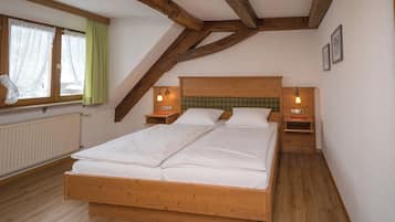 A bedroom with a wooden bed, two bedside tables, a window with curtains, and a radiator.