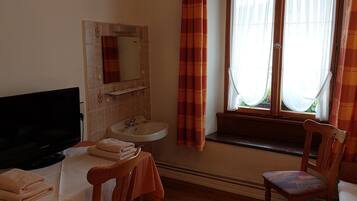 Una habitación con televisión, lavamanos, espejo, ventana con cortinas y una silla.