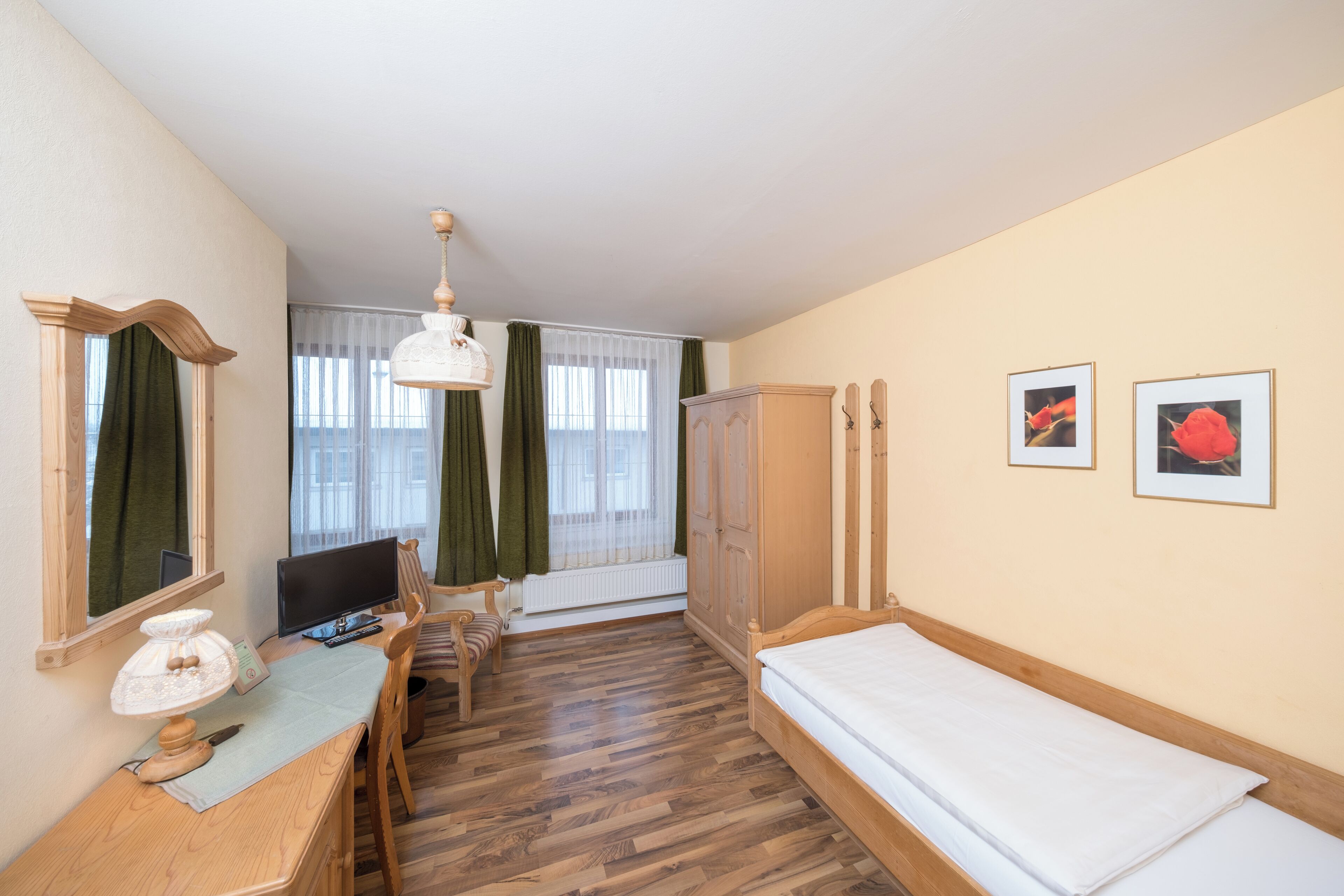 A room with a wooden desk, a bed, a wardrobe, and a window with curtains.