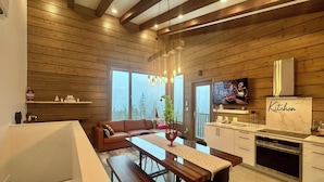 A modern kitchen with wooden beams, a dining area with a bench, and a TV on the wall. - Sunset Lodge - Modern Mountain Luxury - Epic Views - Sleeps 6 (Comox Valley C (Puntledge-B*)