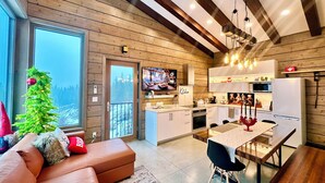 A modern kitchen with wooden cabinetry, a dining area with a table and chairs, and a cozy living room with a sofa and a Christmas tree. - Sunset Lodge - Modern Mountain Luxury - Epic Views - Sleeps 6 (Comox Valley C (Puntledge-B*)