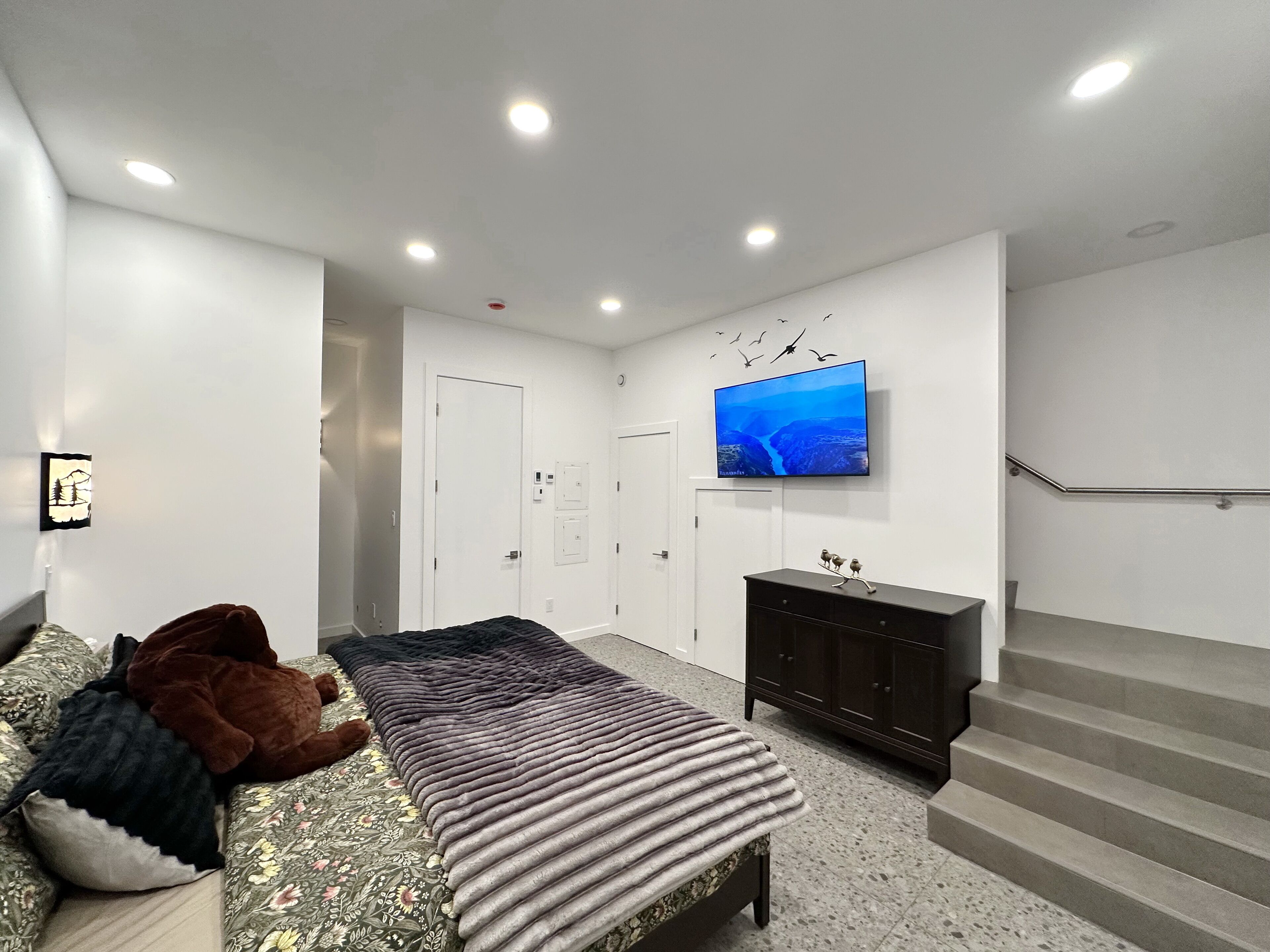 A modern bedroom with a bed, a TV on the wall, a staircase, and a door.