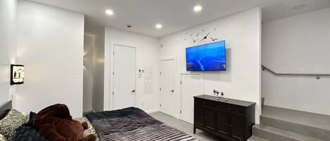 A modern bedroom with a bed, a TV on the wall, a staircase, and a door.