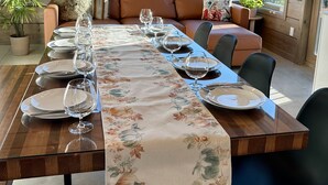 A dining area with a long table set for six, surrounded by wooden walls and large windows offering a view of a forested mountain range. - Sunset Lodge - Modern Mountain Luxury - Epic Views - Sleeps 6 (Comox Valley C (Puntledge-B*)