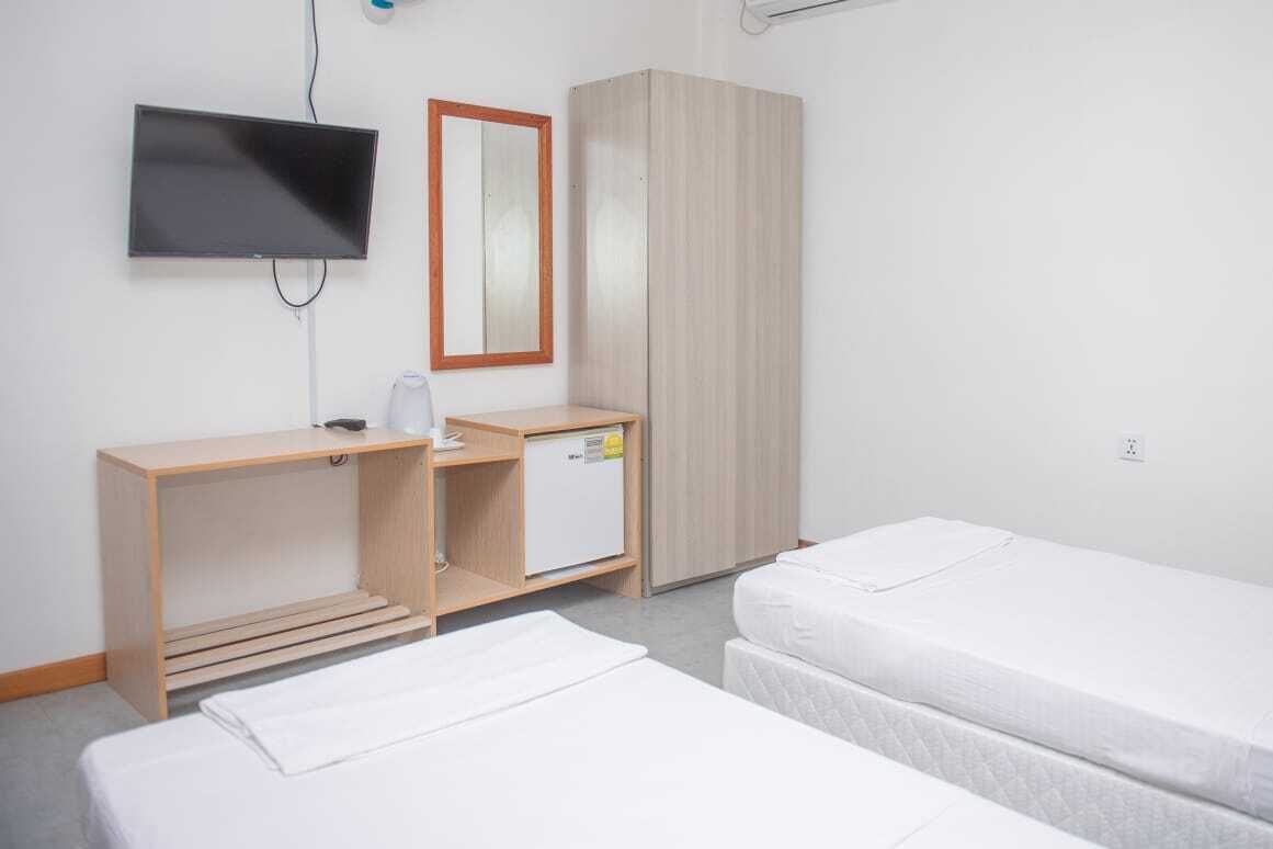 A hotel room with a TV mounted on the wall, a wooden desk with a small refrigerator, and two single beds.