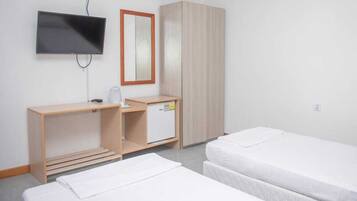 A hotel room with a TV mounted on the wall, a wooden desk with a small refrigerator, and two single beds.