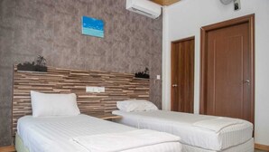A hotel room with two single beds, a wooden headboard, a small table, and a door. - Avanti retreat  (Vaadhoo)