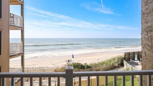 A beachfront view from a balcony with a wooden deck and outdoor furniture.