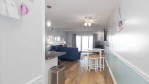 A modern kitchen with a countertop and a built-in oven, a dining area with a table and stools, and a living room with a sofa and a TV.