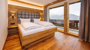 A wooden-framed bedroom with a large bed, a nightstand, and a view of mountains through a sliding glass door. - Kienberg 50 sqm, balcony or terrace, kitchen, 1 bedroom, 1 bed-sitting room, WLAN (Ruhpolding)