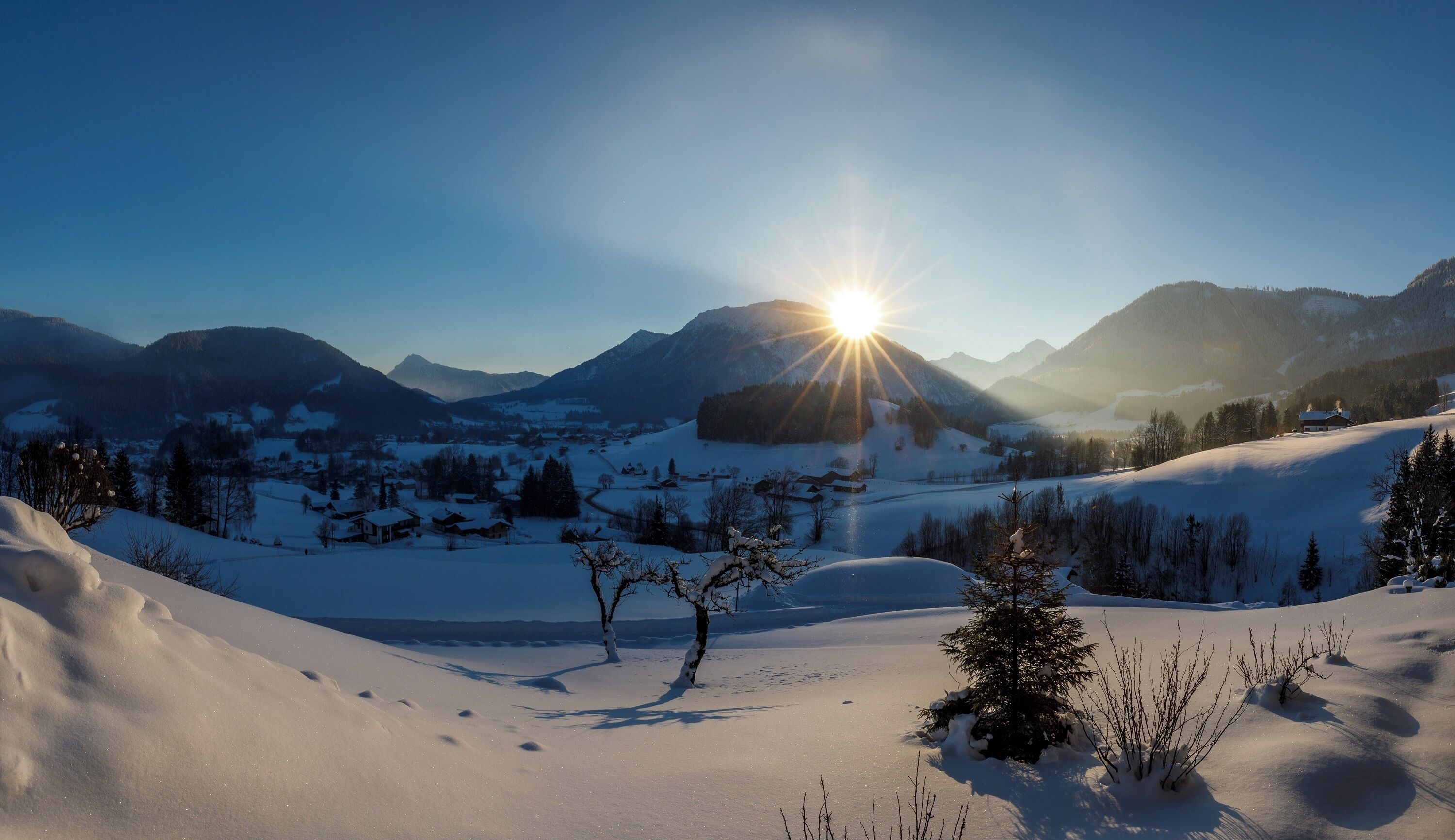 A snowy landscape with a clear sky and mountains in the background.
