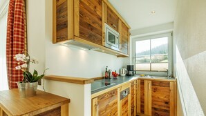 A modern kitchen with wooden cabinets, a microwave, and a window providing a view of the outdoors. - Reifelberg 45 sqm, terrace, kitchen, 1 bedroom, living room, max 3 pers, WLAN (Ruhpolding)