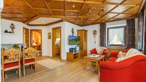 A cozy living room with a wooden ceiling, a red sofa, a wooden dining table with chairs, and a television on the wall. - Zellerberg 45 to 50 sqm, balcony, kitchen, 1 bedroom, living room, 4 pers, WLAN (Ruhpolding)
