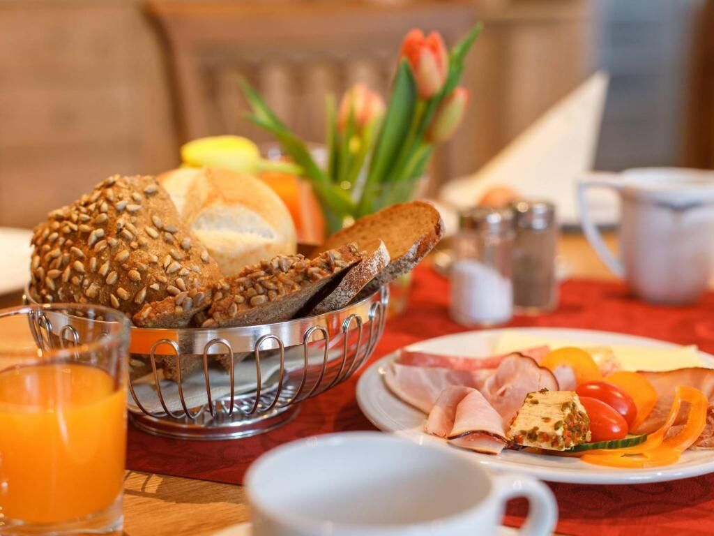 A breakfast setting with a metal bread basket, a plate of sliced meats, and a glass of orange juice.