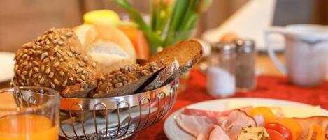 A breakfast setting with a metal bread basket, a plate of sliced meats, and a glass of orange juice.