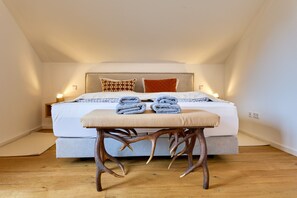 A bedroom with a bed, bedside tables, a bench, and a wooden floor.
