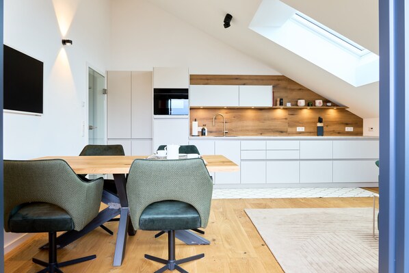 A modern kitchen with a skylight, white cabinets, and a dining area with two chairs.