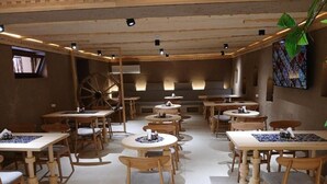 Un restaurante con mesas y sillas de madera, una gran rueda de madera y un mural en la pared.
