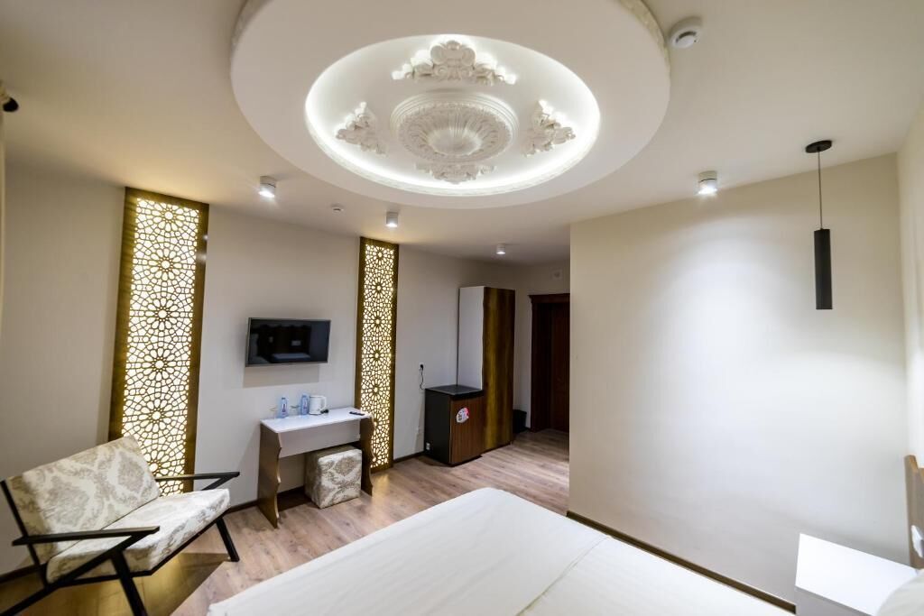 A modern hotel room with a bed, a desk with a chair, a TV, and decorative panels.