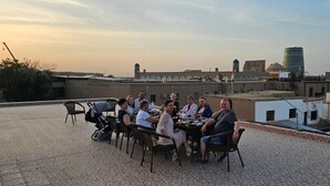 Un grupo de personas cenando en una terraza en la azotea, con vistas a un paisaje urbano.