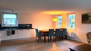 Une cuisine compacte avec un coin repas, comprenant une table et des chaises, une fenêtre avec des stores et un radiateur.