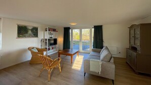 Un salon comprenant un canapé, deux fauteuils, une table basse, une bibliothèque et un téléviseur.
