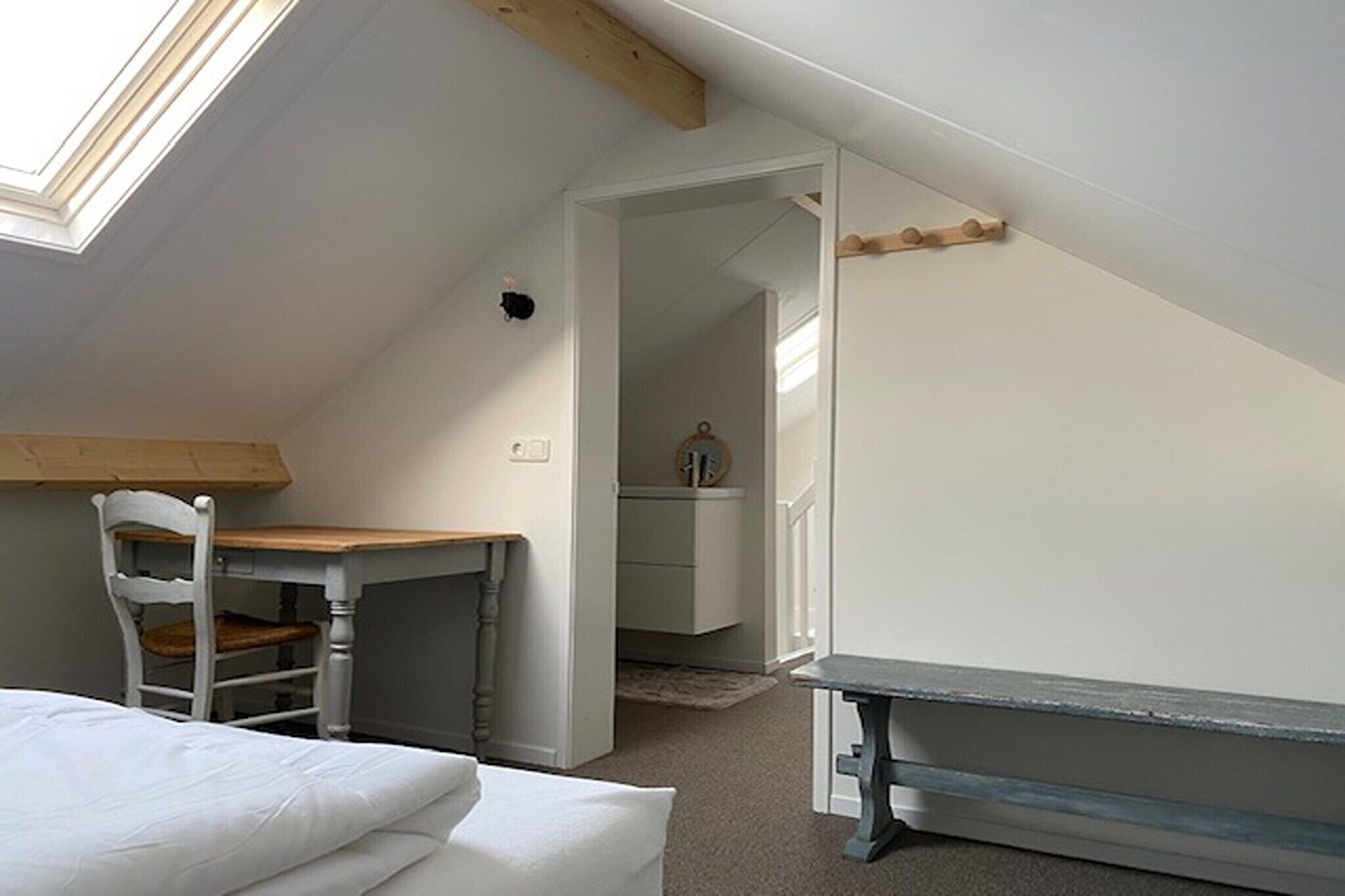 Ein Schlafzimmer mit Oberlicht, einem Holztisch, einem Stuhl, einem Bett und einem kleinen Tisch.