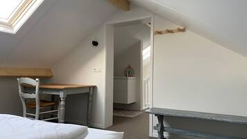Ein Schlafzimmer mit Oberlicht, einem Holztisch, einem Stuhl, einem Bett und einem kleinen Tisch.