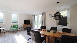 Ein Essbereich mit einem Holztisch, schwarzen Stühlen, einem grünen Stuhl und einer schwarzen Pendelleuchte.