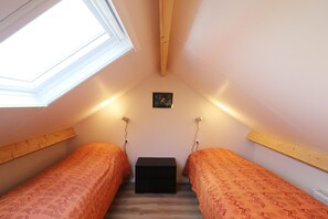 Een compacte, goed verlichte slaapkamer onder de dakrand met twee eenpersoonsbedden, een dakraam en een kleine, zwarte opbergkist.