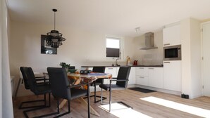 Eine moderne Küche mit Essbereich, inklusive rundem Tisch mit Stühlen, einer Pendelleuchte und einem Fenster über der Spüle.