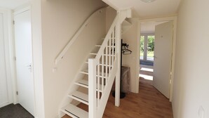 Eine Treppe führt zu einer oberen Etage, eine Tür links und ein Blick ins Freie durch eine offene Tür.