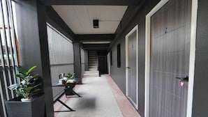 A corridor with a staircase, a door with a lock, and potted plants. - Cozy Standard Single in Huai Kwang (Bangkok)