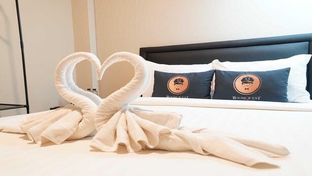 A neatly made bed with two pillows featuring a uniform design, a headboard, and a bedside table with a lamp. - Cozy Standard Single in Huai Kwang (Bangkok)
