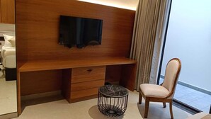 Una habitación de hotel moderna con un escritorio de madera, un televisor montado en la pared, una pequeña mesa redonda y una silla acolchada.